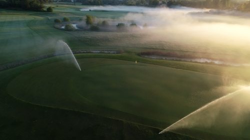 Golfbana täckt i dimma i en solnedgång.