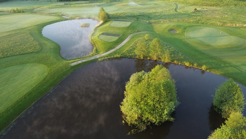 Översikt på en golfbana med vatten och träd som hinder.